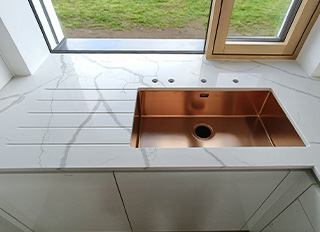 měděný dřez s vyfrézovanou odkapovou plochou do bíle kuchyňské desky z umělého kamene Technistone Crystal Calacatta Silva