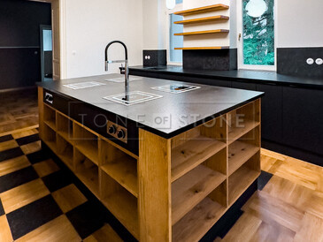 Pracovní deska kuchyňského ostrůvku ze žuly Nero Assoluto Zimbabwe (trattato). Součástí ostrůvku jsou 4 varné desky s horní montáží a baterií uprostřed. 