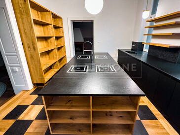 Pracovní ostrůvek ze žuly Nero Assoluto  Zimbabwe (trattato) s osazenými 4 varnými deskami s horní montáží a baterií uprostřed. Ze stejného přírodního kamene je i pracovní deska v pozadí.  