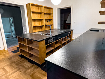 Detail kuchyňské pracovní desky ze žuly Nero Assoluto Zimbabwe (trattato), v pozadí varný ostrůvek ze stejného materiálu. Zakázková výroba TONE OF STONE. 