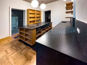 Detail kuchyňské pracovní desky ze žuly Nero Assoluto Zimbabwe (trattato), v pozadí varný ostrůvek ze stejného materiálu. Zakázková výroba TONE OF STONE. 