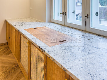 Kuchyňská pracovní deska z indické žuly Colonial White v úpravě satén. Do kuchyňské desky je vsazen dřez se spodní montáží a zabudovaný projektor. Integrovaný parapet s průduchy pro proudění teplého vzduchu z topení je součástí pracovní desky. Zakázková výroba TONE OF STONE.     