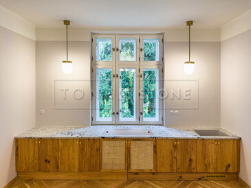 Kuchyňská desku ze žuly Colonial White v úpravě satén. Do desky je vsazen dřez se spodní montáží, zabudovaný projektor a integrovaný parapet s průduchy pro proudění teplého vzduchu. Zakázková výroba TONE OF STONE.  