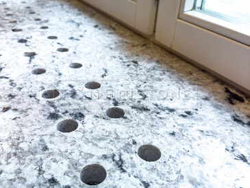 Detail průduchů pro proudění teplého vzduchu, které jsou součástí pracovní desky a integrovaného parapetu ze žuly Colonial White. Zakázková výroba TONE OF STONE.  