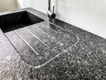 Kuchyňská pracovní deska - žula STEEL GREY, kartáčovaný povrch, lepený kamenný dřez, odkapová plocha včetně drážek, usazení varné desky do roviny. Zakázková výroba TONE OF STONE.