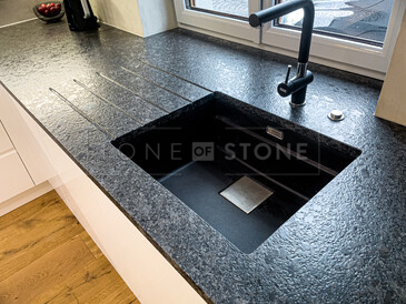 Detail dřezu v kuchyňské desce ze žuly STEEL GREY v kartáčovaném povrchu, vyfrézované odkapové drážky, vsazený dřez, vsazená varná deska. Zakázková výroba TONE OF STONE.  Detail dřezu v kuchyňské desce ze žuly STEEL GREY v kartáčovaném povrchu, vyfrézované odkapové drážky, vsazený dřez, vsazená varná deska. Zakázková výroba TONE OF STONE.