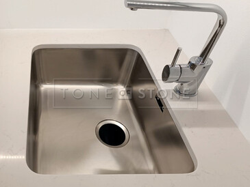 Detail na dřez se spodní montáží a výřez pro baterii v kamenné kuchyňské desce z materiálu Technistone Noble Supreme White. Zakázková výroba TONE OF STONE.