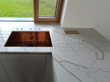 Rohový spoj kuchyňské desky z Technistone Crystal Calacatta Silva, jejíž součástí je i integrovaná elektrická zásuvka a měděný dřez se spodní montáží. Zakázková výroba TONE OF STONE.