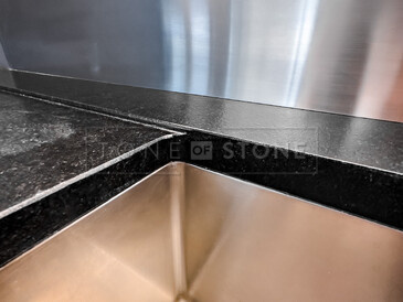 Detail osazení dřezu se spodní montáží do žulové kamenné desky z přírodního kamene Nero Assoluto Zimbabwe. Součástí je i vyfrézovaná odkapová plocha. Zakázková výroba TONE OF STONE.