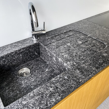 Kuchyňská pracovní deska - žula STEEL GREY, kartáčovaný povrch, lepený kamenný dřez, odkapová plocha včetně drážek, usazení varné desky do roviny. Zakázková výroba TONE OF STONE. 