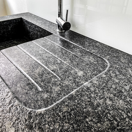 Kuchyňská pracovní deska - žula STEEL GREY, kartáčovaný povrch, lepený kamenný dřez, odkapová plocha včetně drážek, usazení varné desky do roviny. Zakázková výroba TONE OF STONE.