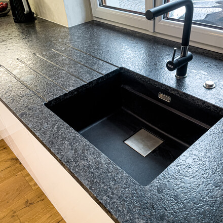 Detail dřezu v kuchyňské desce ze žuly STEEL GREY v kartáčovaném povrchu, vyfrézované odkapové drážky, vsazený dřez, vsazená varná deska. Zakázková výroba TONE OF STONE. 