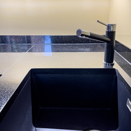 Kuchyňská pracovní deska z přírodního kamene - leštěná černá žula s třpytivými fragmenty - STAR GALAXY, detail přisazeného spodního dřezu a baterie Kuchyňská pracovní deska z přírodního kamene - leštěná černá žula s třpytivými fragmenty - STAR GALAXY, detail přisazeného spodního dřezu a baterie